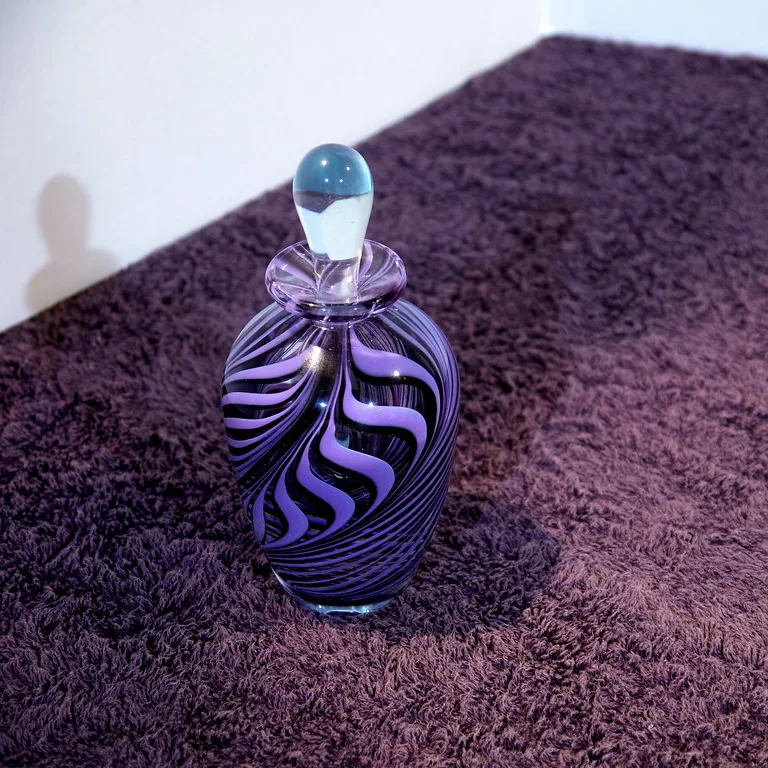 La photo de départ : un flacon en verre soufflé aux spirales violettes, posé sur une moquette