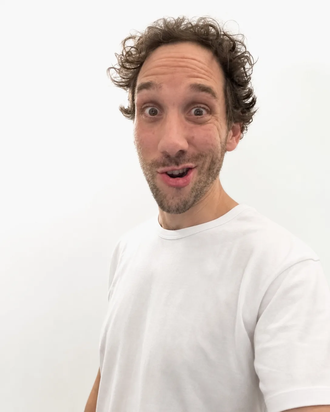 Ismael l'air très surpris, yeux grands ouverts, t-shirt blanc, sur fond blanc