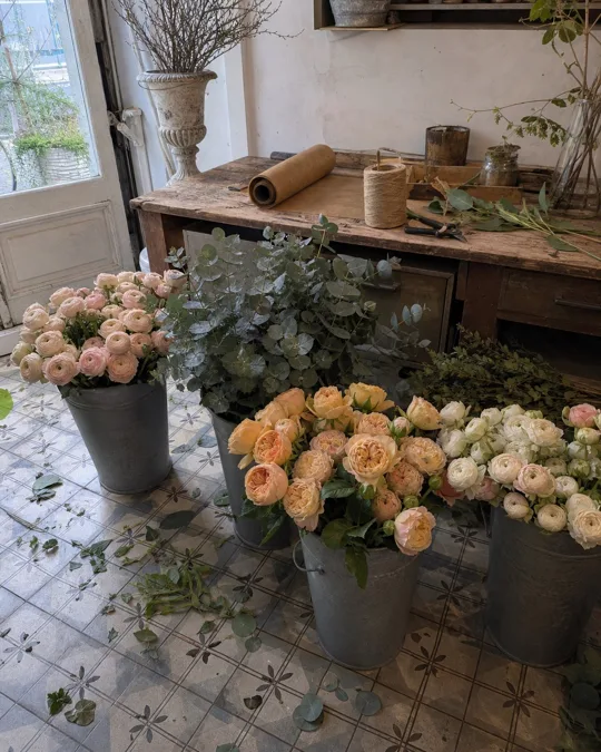 Photo de départ : fleuriste, la caméra monte au-dessus des seaux de fleurs du matin et découvre la table de travail : papier kraft, ficelle, sécateur