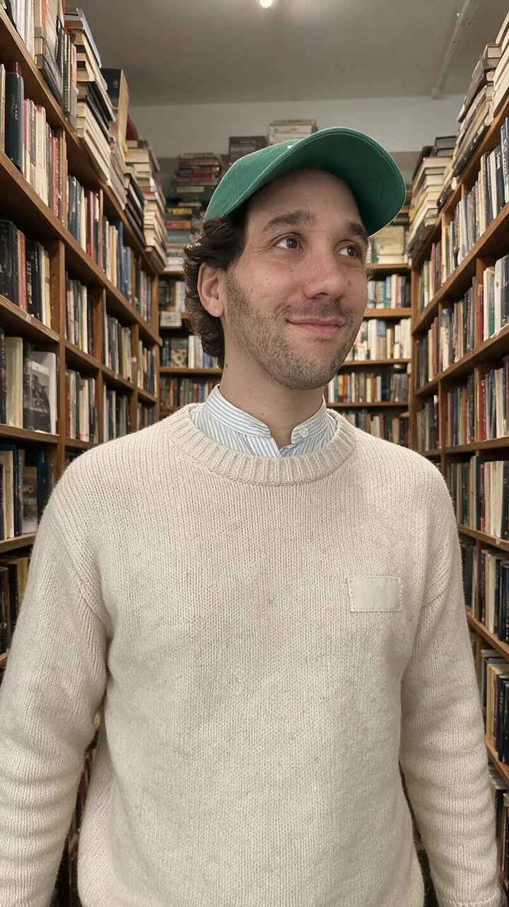 La retouche de la libraire : Ismael entre les rayons d'une librairie, en pull en maille écrue, avec la pose et le cadrage de sa photo
